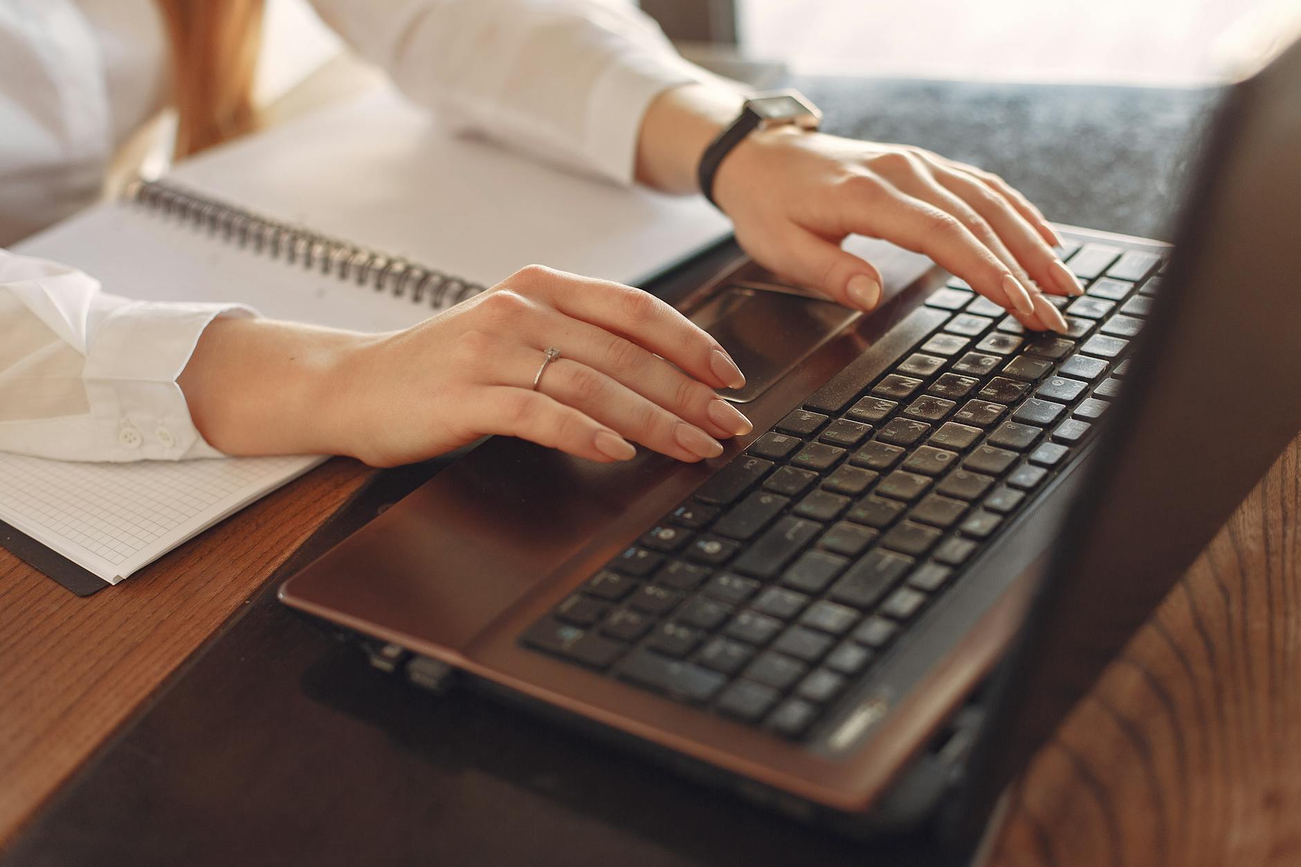 Close-up of a person typing on a laptop with a notebook nearby, ideal for remote work concepts.